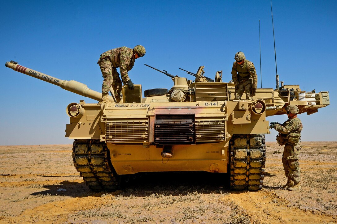 Three soldiers stand on or near a tank while inspecting it.