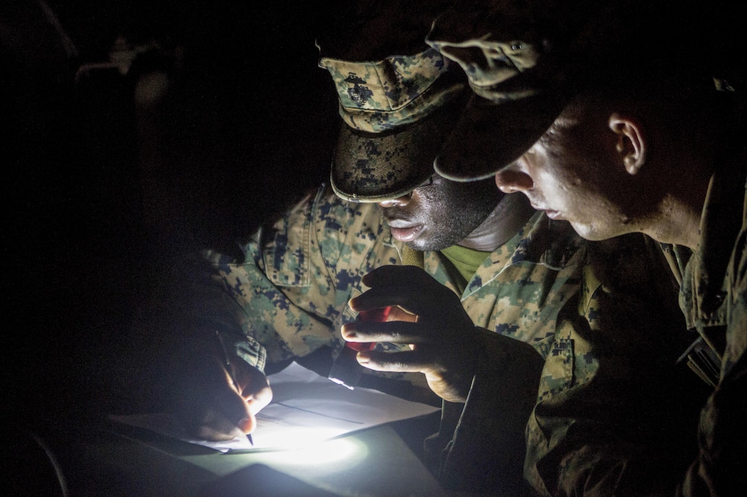 Two Marines look over notes by flashlight.