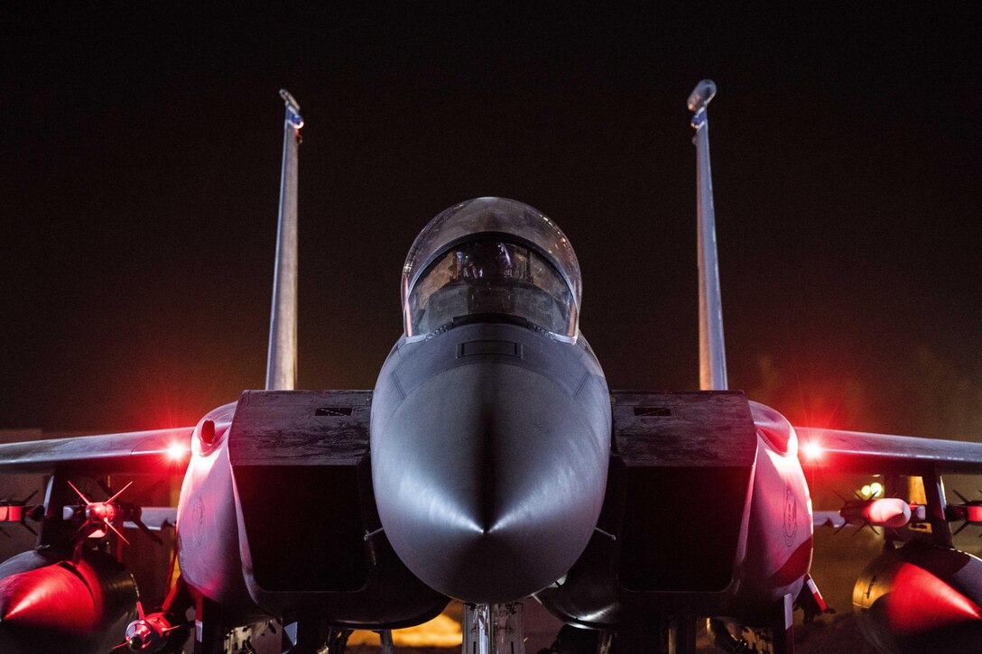 An airman works in the cockpit of an aircraft on a dark flightline.