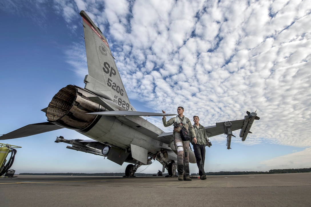 Two airmen walk around an aircraft on a flightline.