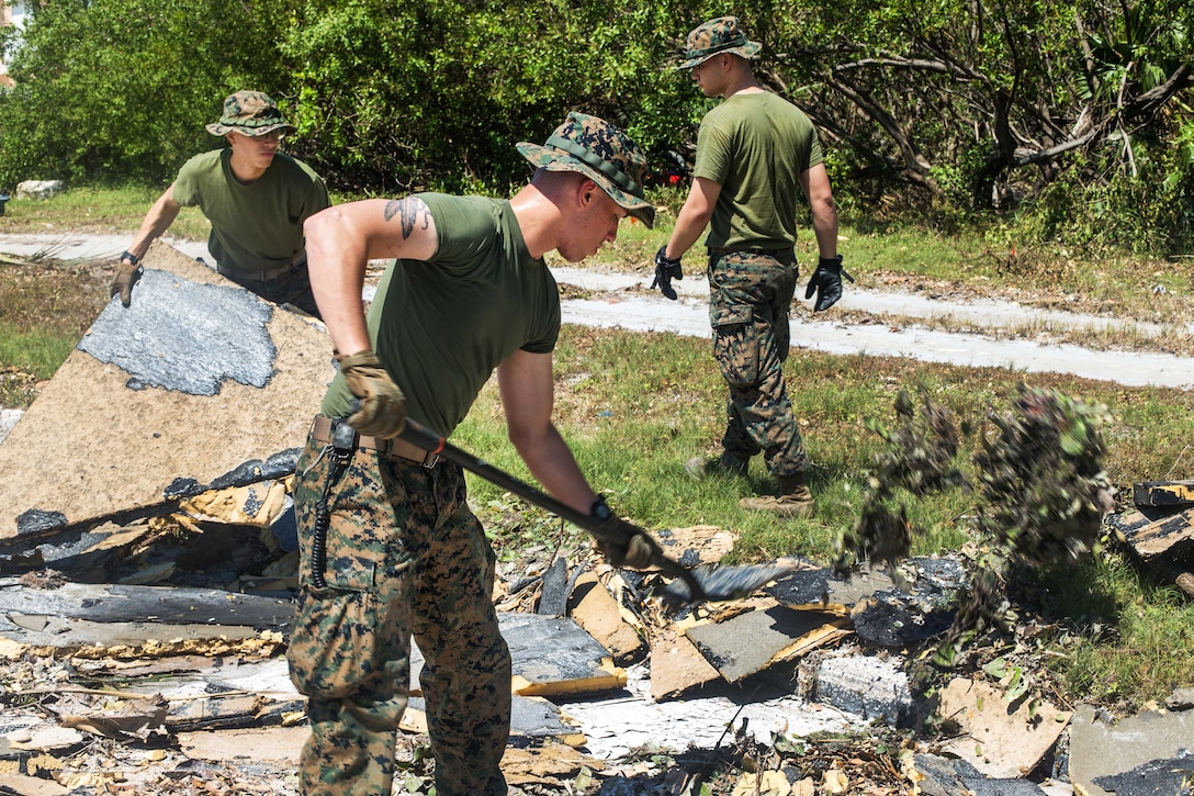 Three Marines shovel debris off a grassy area.