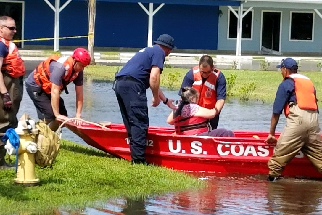 Members of the Coast Guard help a woman into a boat.