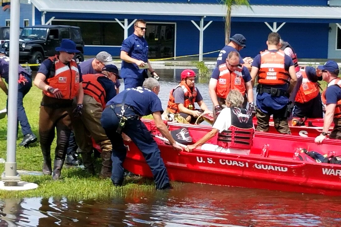 Members of the Coast Guard assist civilians into boats.