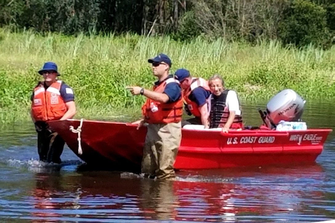 A Coast Guard team assists pulls a boat with a woman through water.