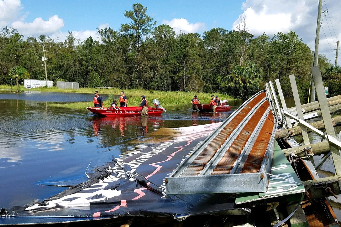 Members of the coast guard pull boats though floodwaters.