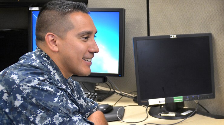 A sailor sits at a desk in front of a computer talking.