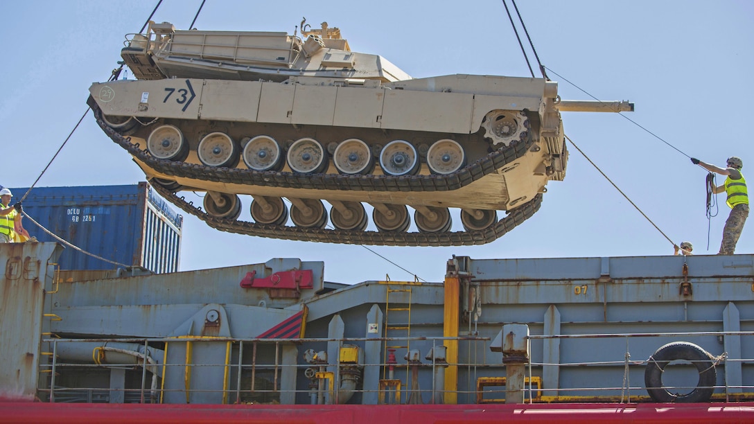 Soldiers lower a tank suspended in the air.