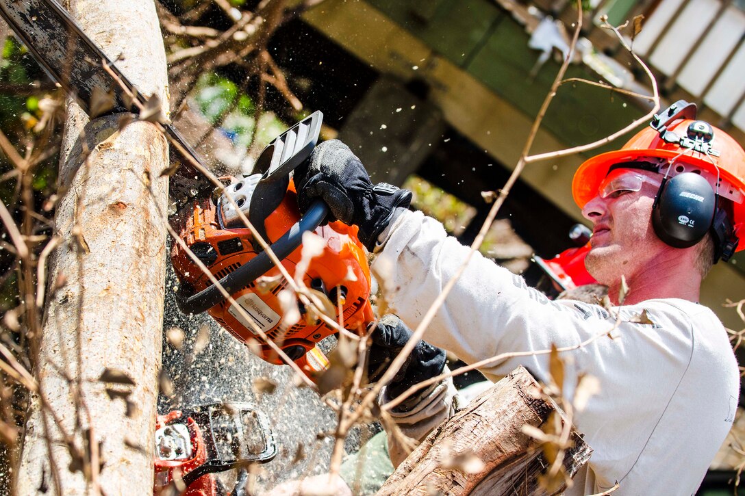 A soldier uses a chainsaw to clear debris.