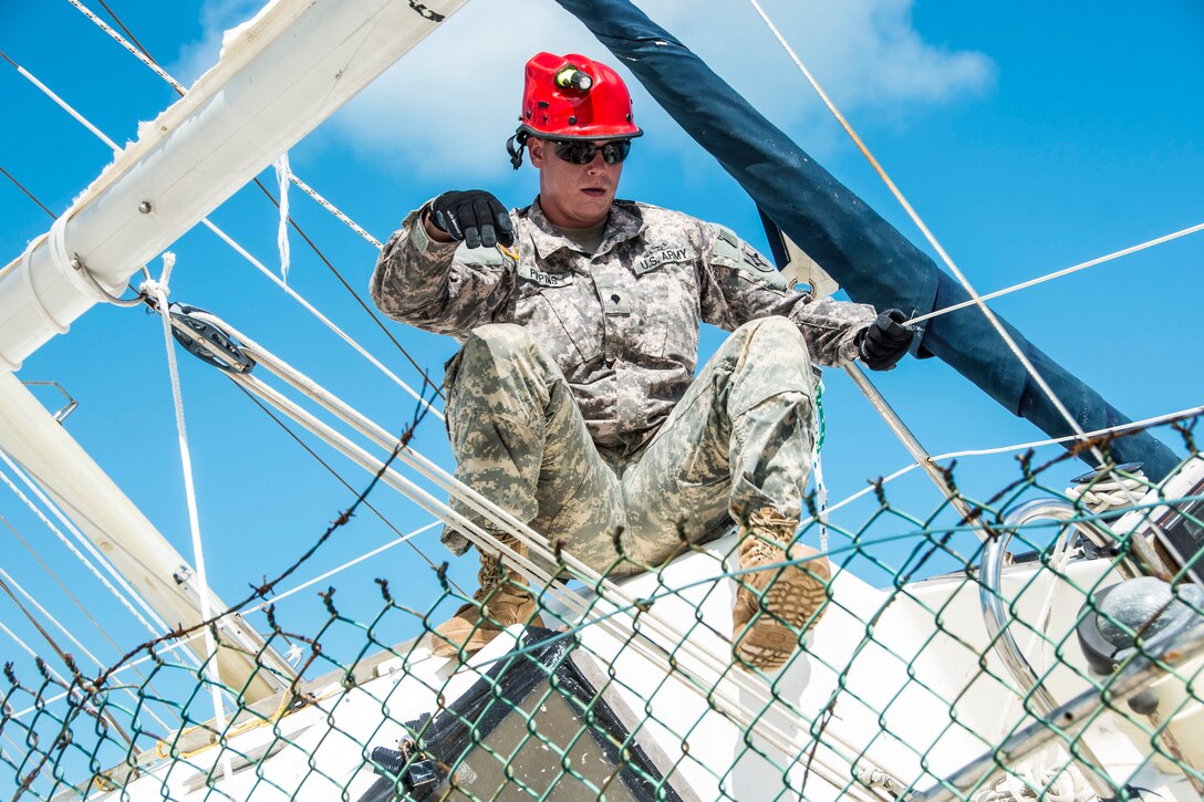 A soldier climbs on top of a sailboat lodged in a fence.