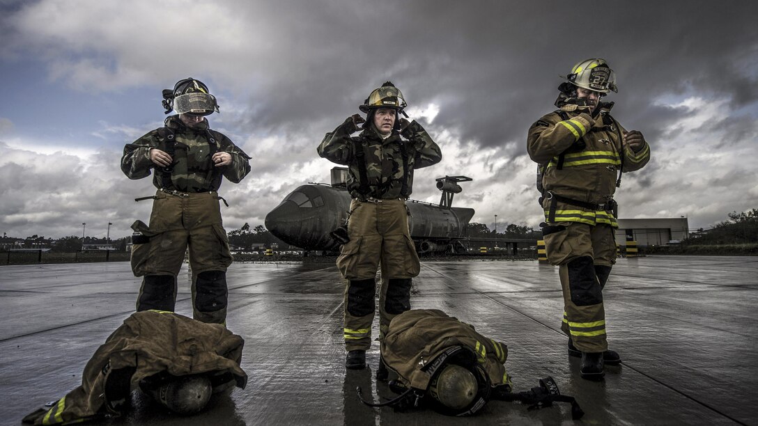 Three firefighters don protective gear on a flightline.