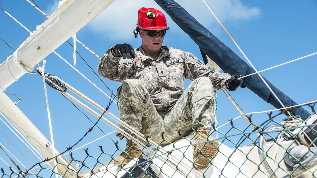 A soldier climbs on a boat stuck in a fence.