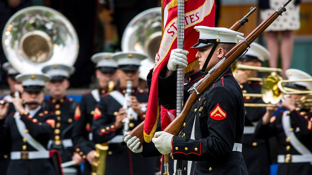 Marines march in formation as fellow Marines play instruments.