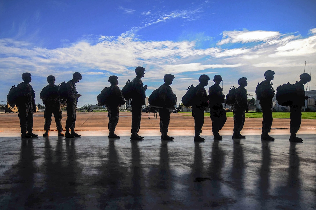 Soldiers, shown in silhouette, line up on a flightline.