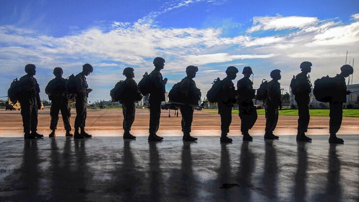 Soldiers, shown in silhouette, line up on a flightline.