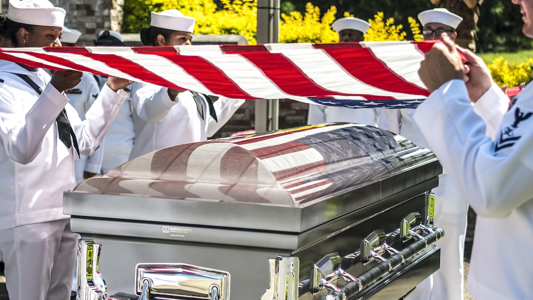 Sailors hold a U.S. flag over a casket.