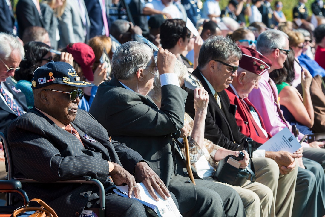 A group of people including veterans listen to a speech.