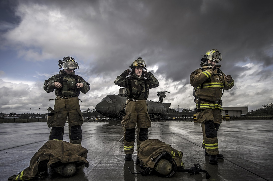 Three firefighters don protective gear on a flightline.