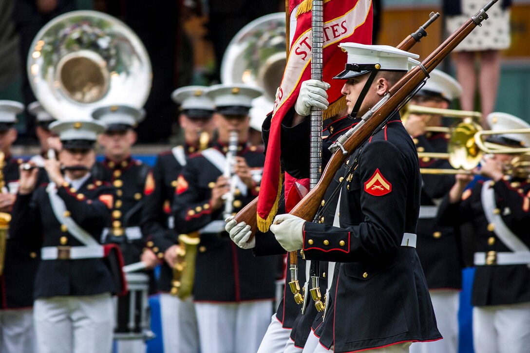 Marines march in formation as fellow Marines play instruments.