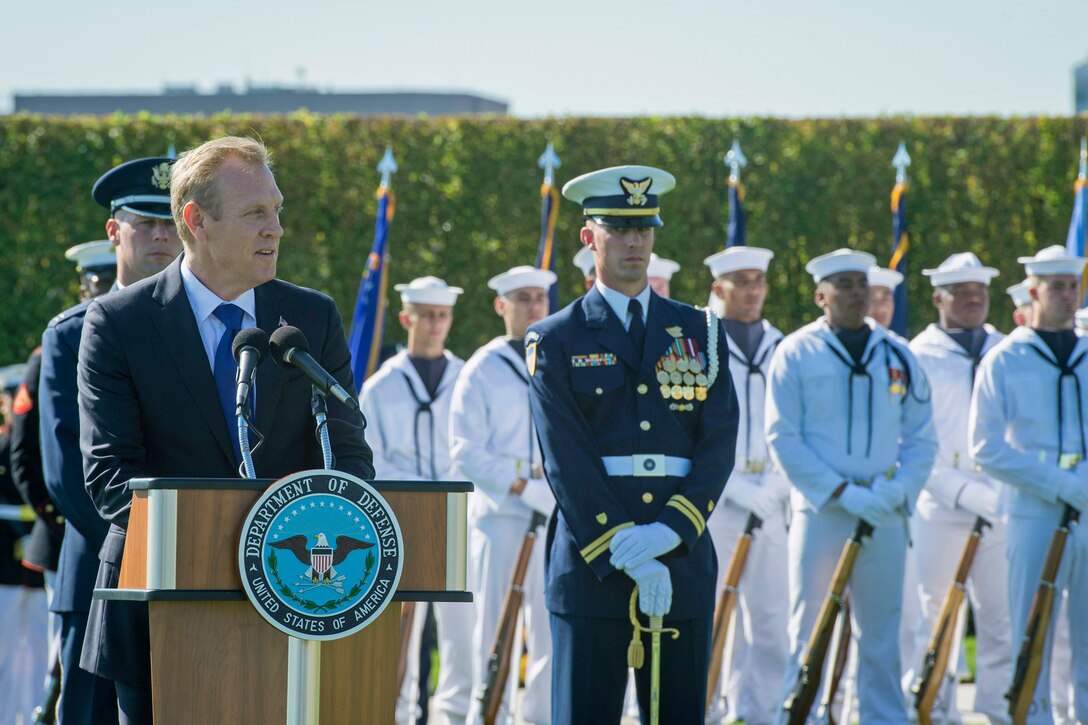 Deputy Defense Secretary Pat Shanahan speaks from behind a podium with service members behind him.