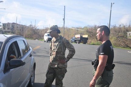 A Virgin Islands National Guard member stands by the window of a civilian vehicle with a member of the Virgin Islands Police Department.