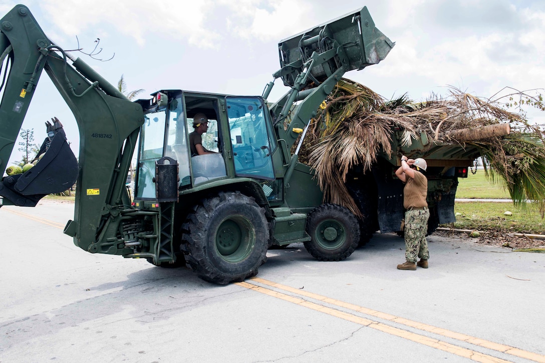 A sailor guides another sailor operating a backhoe to remove branches and trees felled by Hurricane Irma.