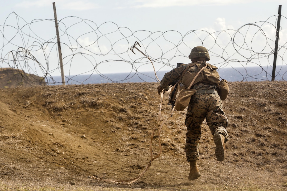 A Marine throws a grappling hook to breach through a barbed wire obstacle.