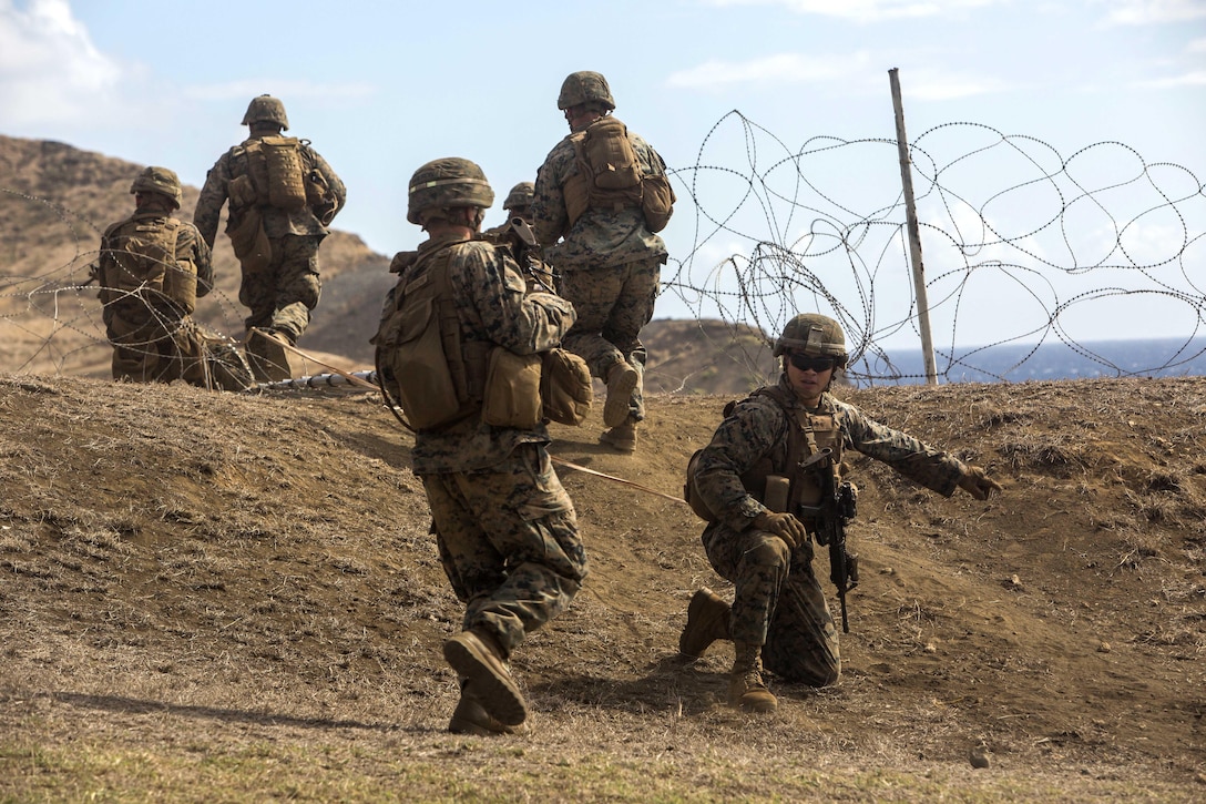 Marines breach through a barbed wire obstacle during an advanced infantry course.