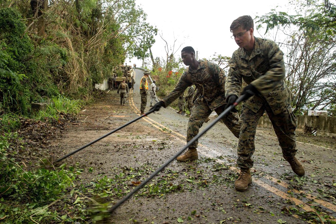 Marine Cpls. Marcel T. Trice, left, and Anthony J. Guiliano III clear out debris from a roadway.