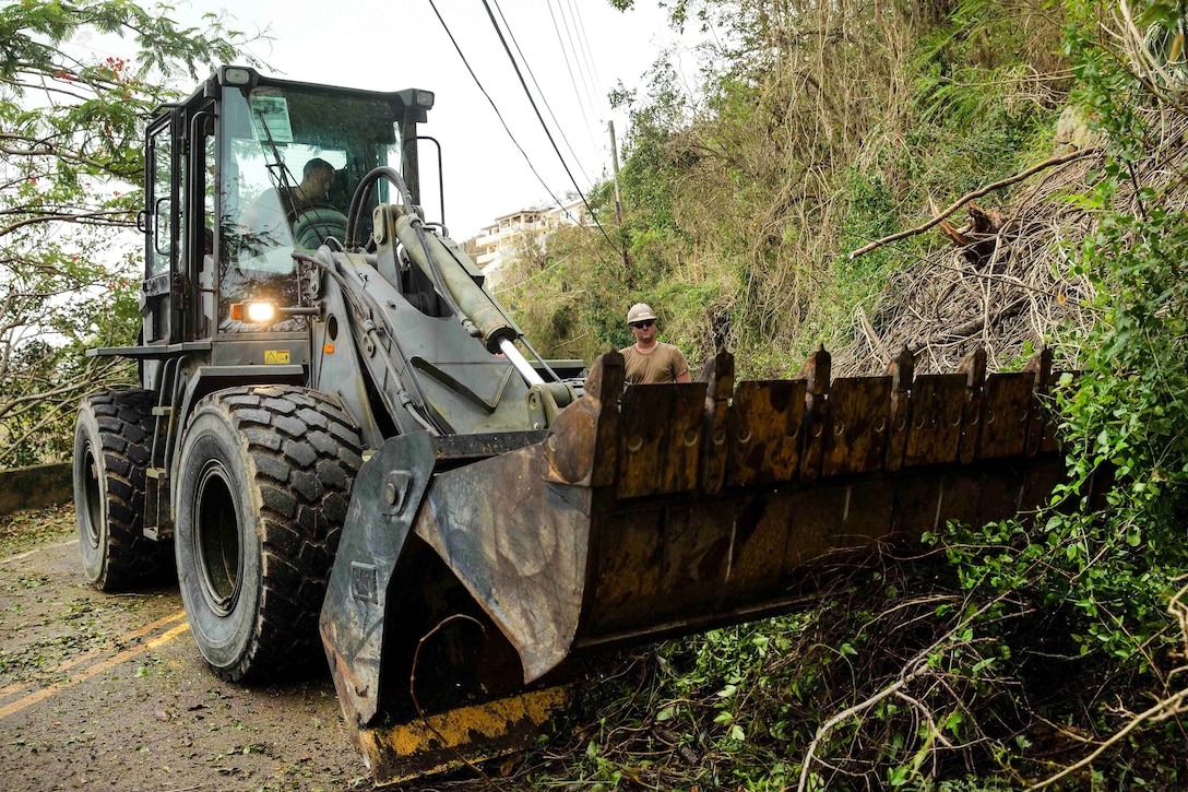 A sailor operates a bulldozer clearing debris from the roadway.