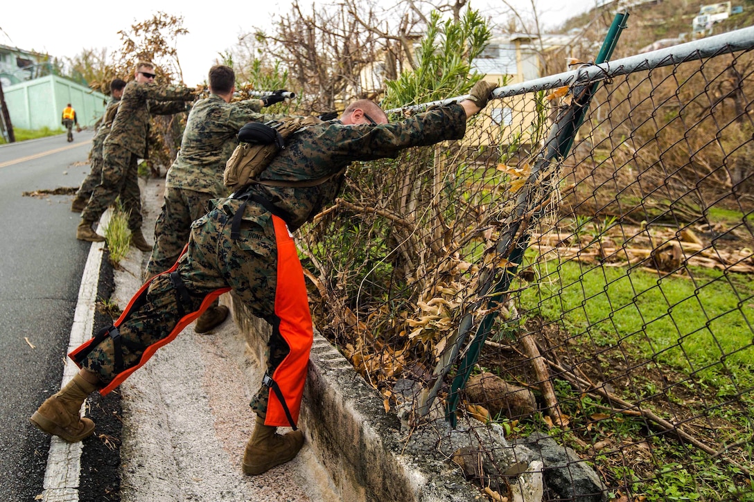 Marines push a fence to clear the debris from a roadway.