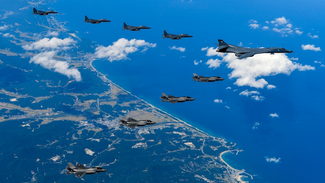 Nine aircraft fly over coastline in a "V" formation.