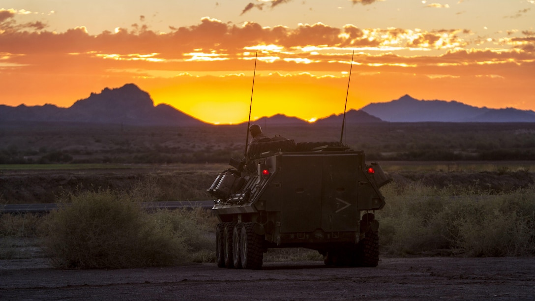 An armored vehicle faces a view of an orange sky with the sun behind purplish-blue mountains.