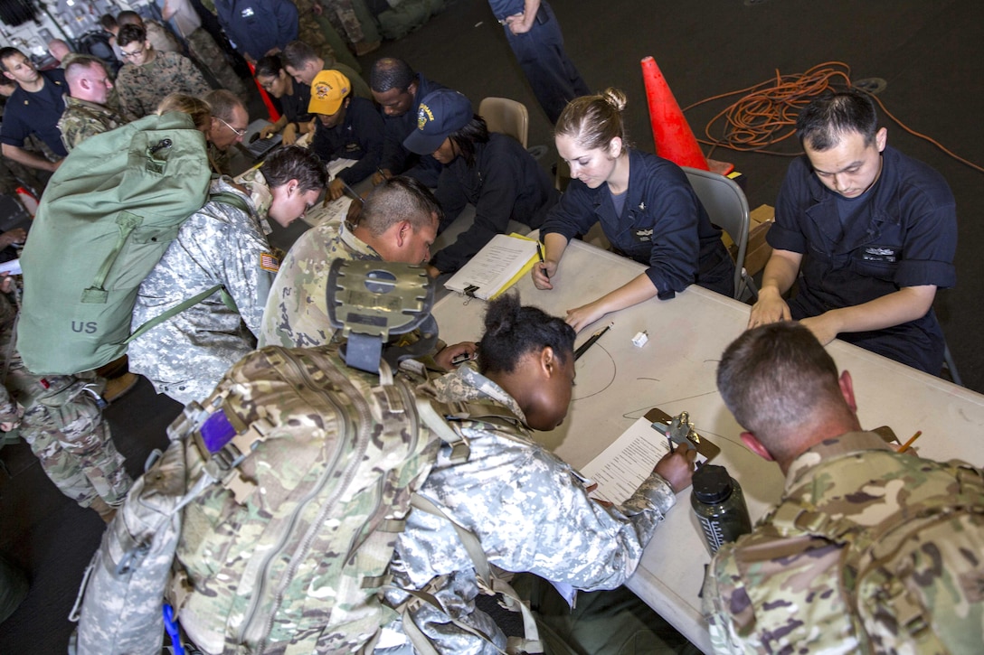 Service members lean over tables writing on papers.