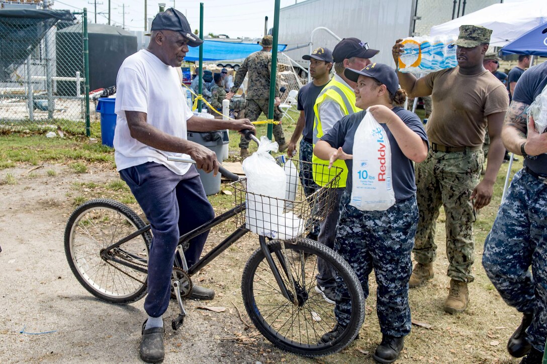 A sailor hands ice to a person on a bike.