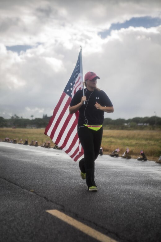 A run participant carries an American flag during the Fisher House Hero and Remembrance Run, Walk or Roll 8kon Ford Island aboard Joint Base Pearl Harbor-Hickam, Sept. 9, 2017. The road was adorned with over 7,500 military boots decorated with American flags, name tags with a photo of the service member, and information on the combat tour they were serving or where they were stationed. The free event was open to the public and military to honor those we have lost in the service since Sept. 11, 2001. (U.S. Marine Corps photo by Sgt. Zachary Orr)