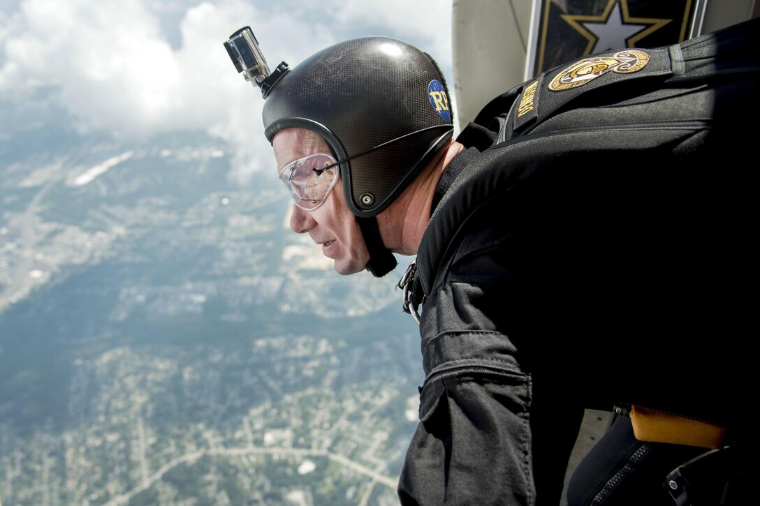 A soldier wearing a helmet and goggles looks out from an open aircraft door.