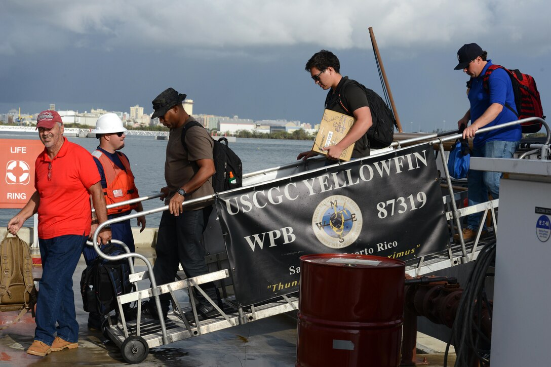 A row of civilians leaves a ship with a member of the Coast Guard watching.