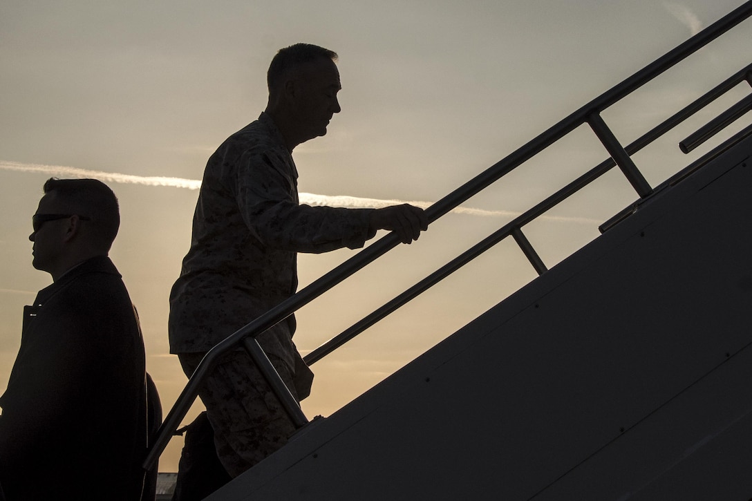 The chairman of the Joint Chiefs, shown in silhouette, climbs the stairs to an aircraft.