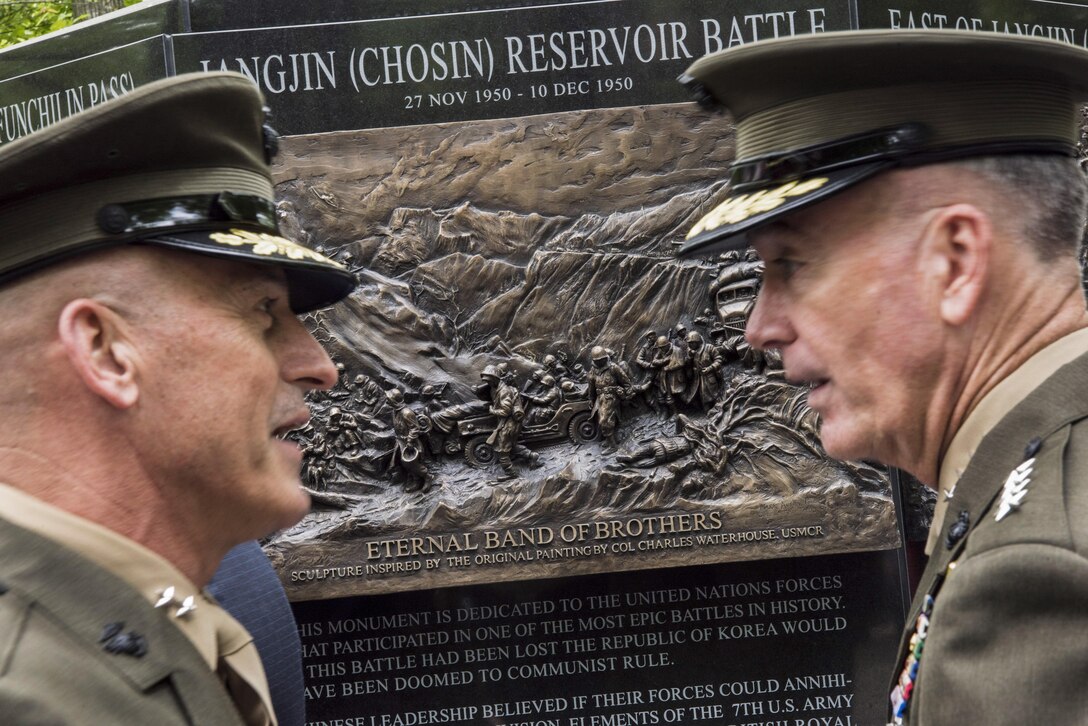 The chairman of the Joint Chiefs talks to another Marine at a monument.