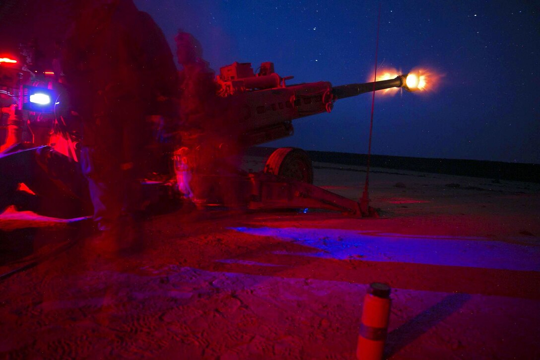 Marines fire a howitzer at night.