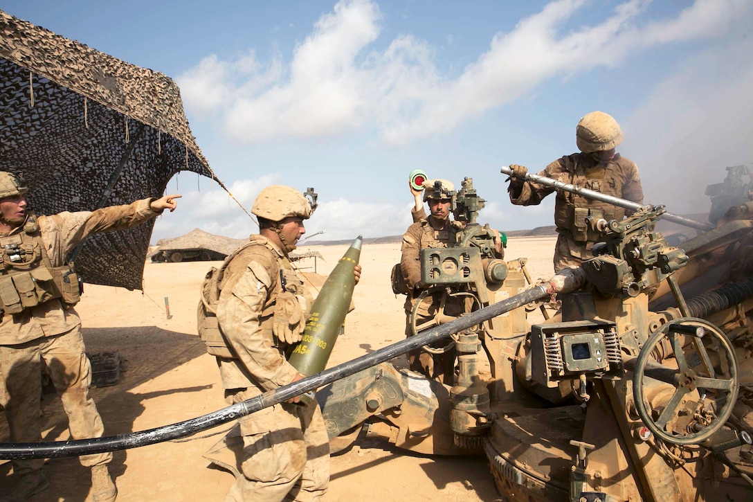 A Marine walks toward a howitzer with a round.