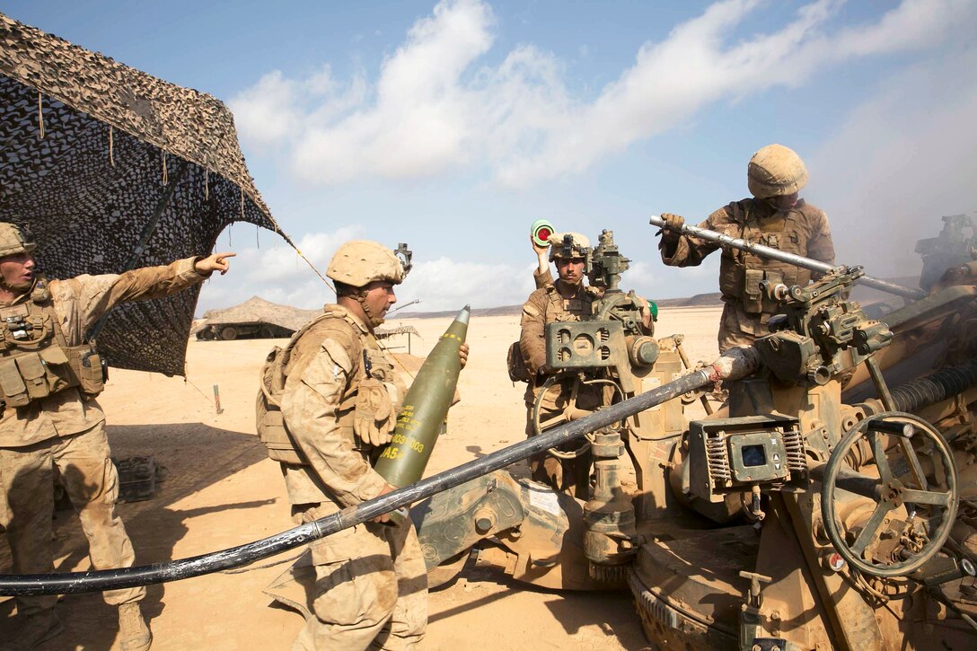 A Marine walks toward a howitzer with a round.