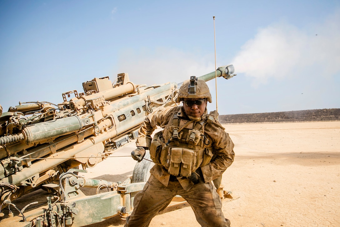A Marine pulls lanyard to fire a howitzer.
