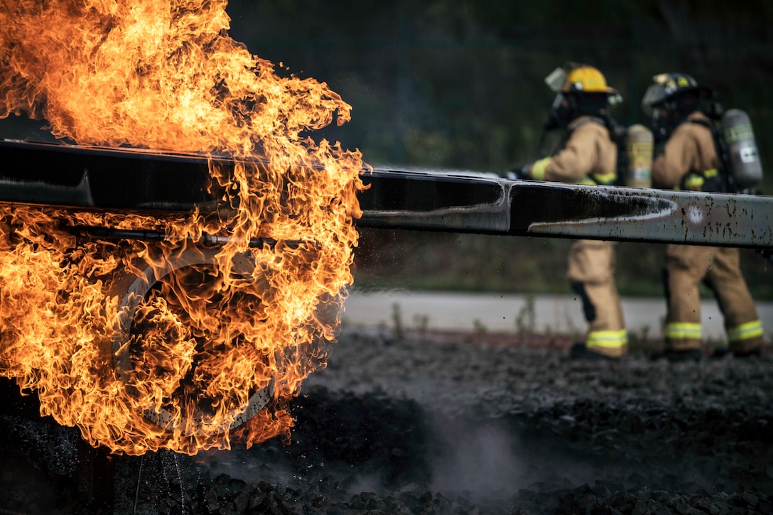 Two firefighters position themselves near a fire.