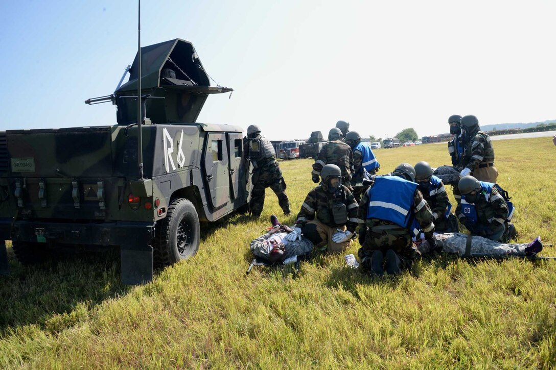 A military vehicle sits next to a group of people kneeling around other people on the ground.