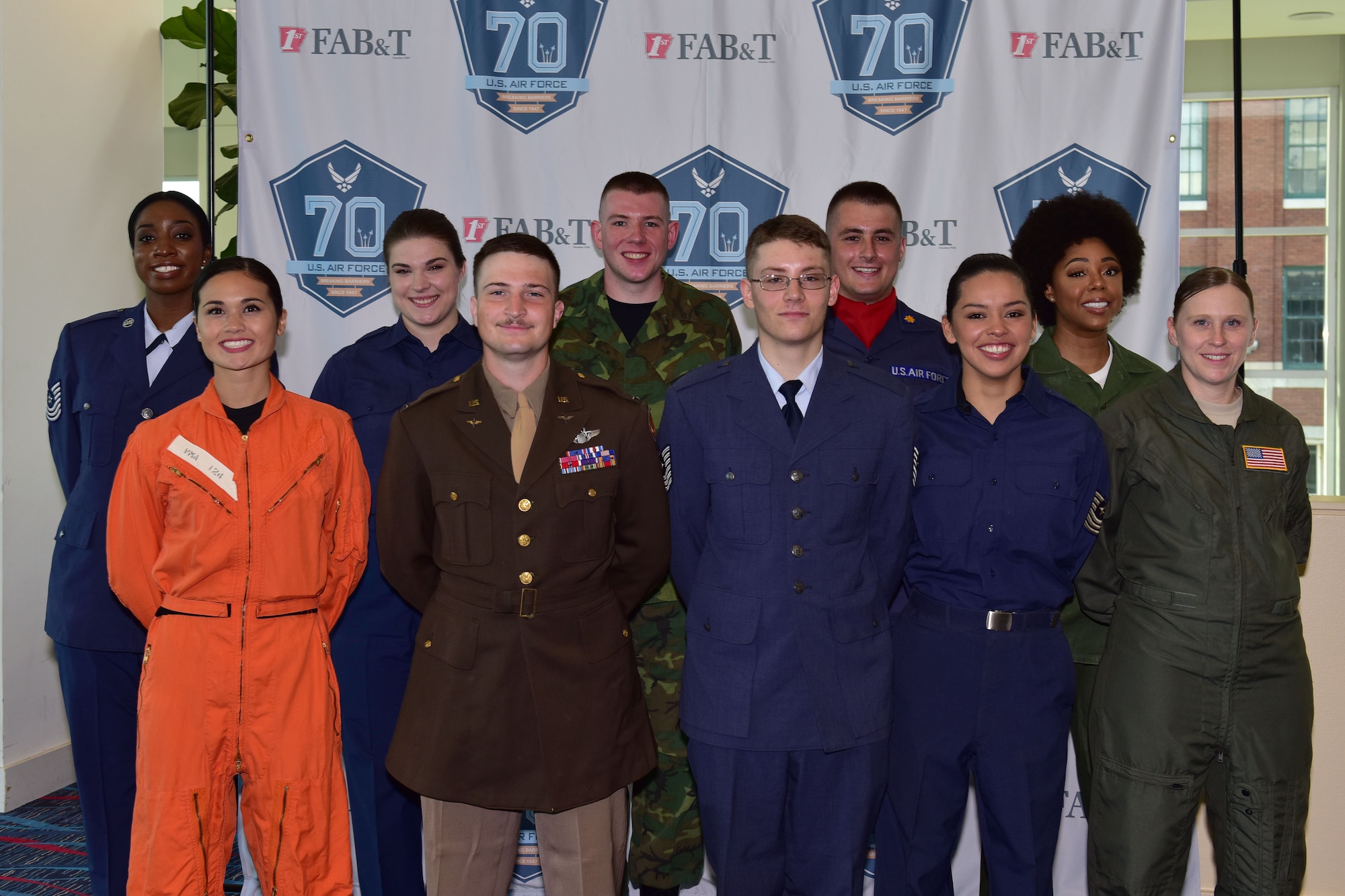 A group of people stand in front of a background wearing different historic U.S. Air Force uniforms.