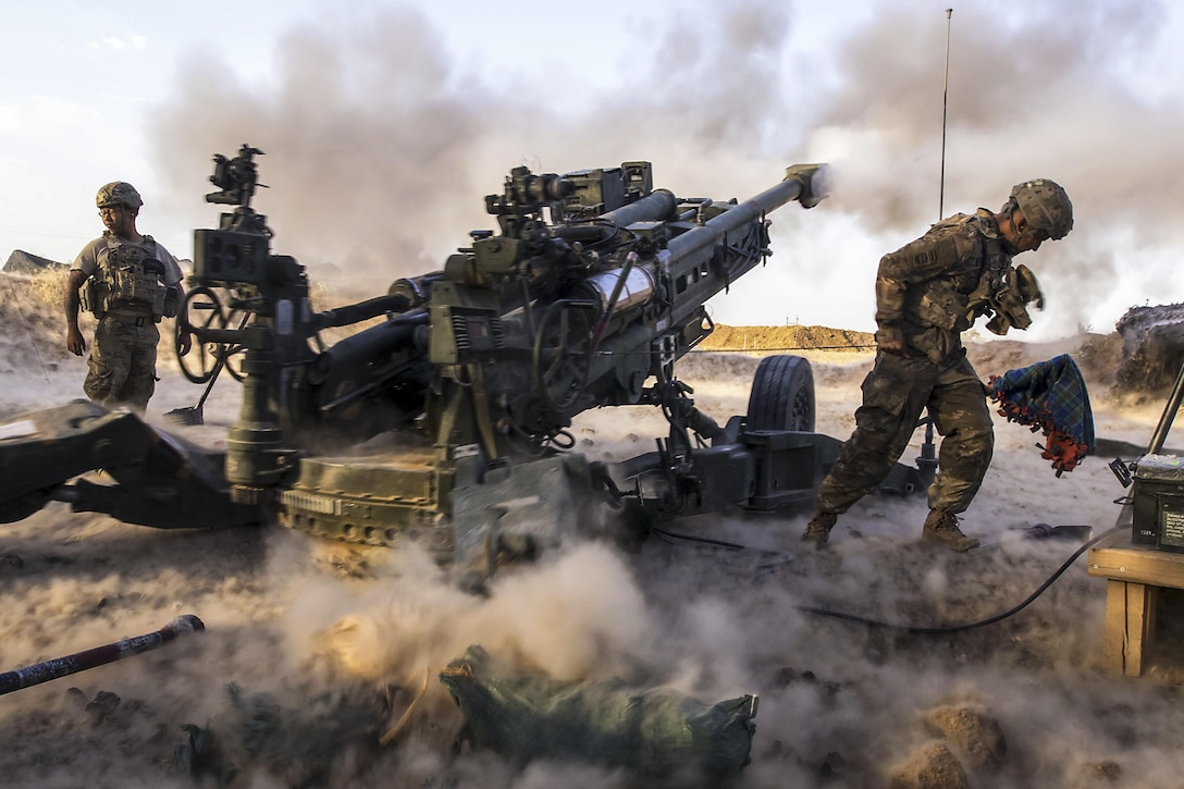Soldiers fire an artillery weapon, creating clouds of smoke.