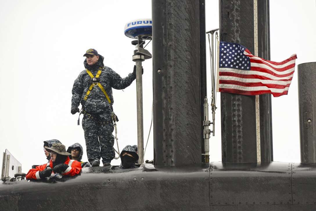 A sailor stands atop a submarine and looks into the distance.