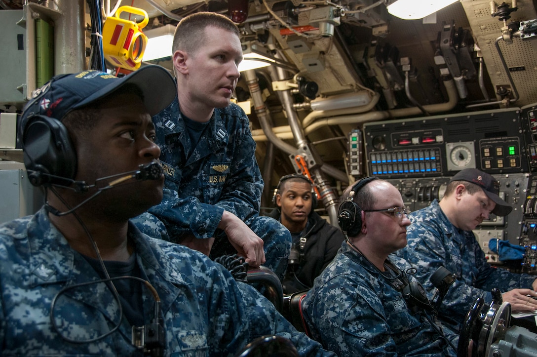 A group of sailors in an interior space on a submarine look out of the frame.