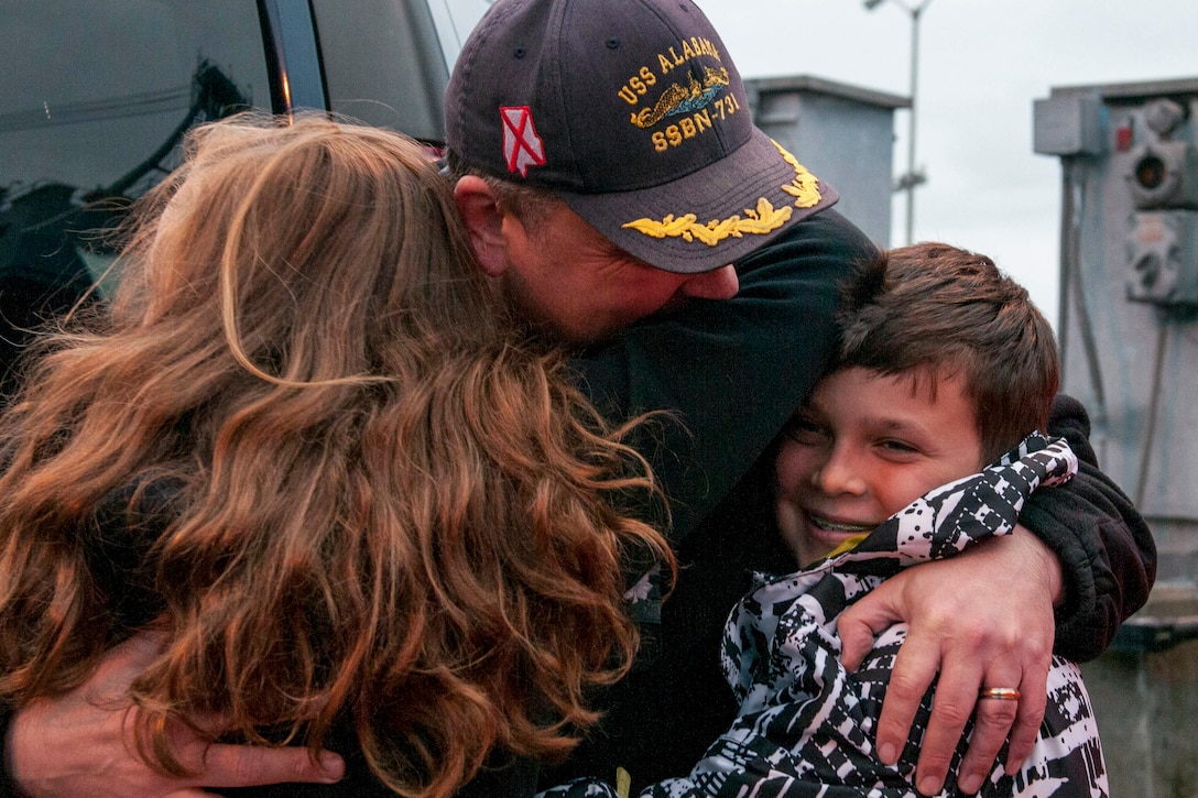 A sailor embraces a woman and a smiling child.